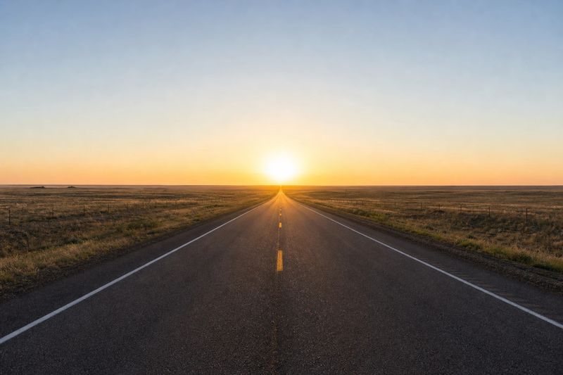 A two-lane highway running straight towards the horizon under a wide open sky