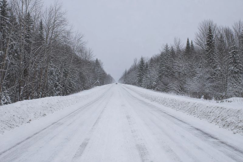 A snow-covered two-lane road running between plowed banks toward low winter hills